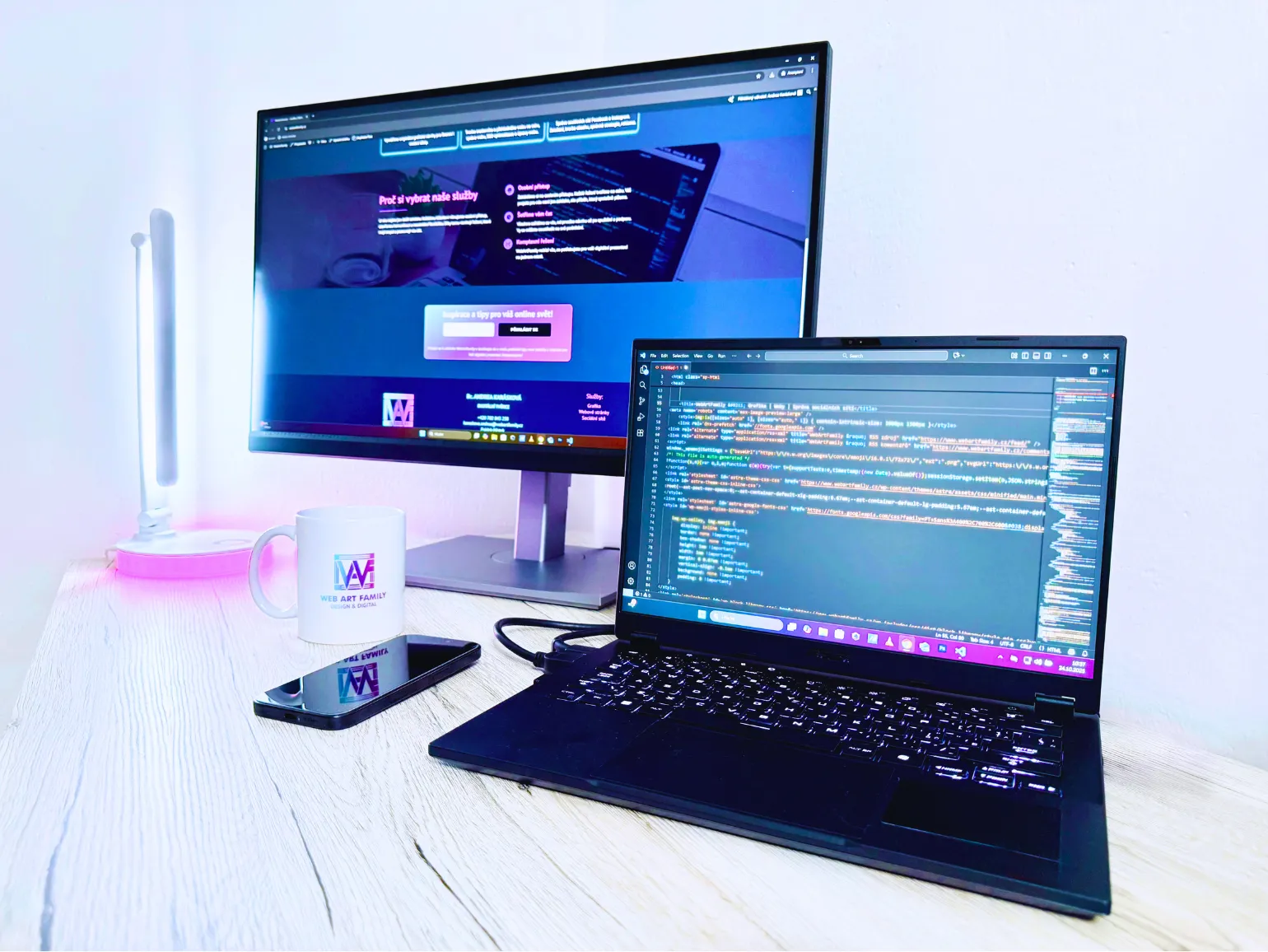 Moderní workspace WebArtFamily – tvorba webových stránek, programování na notebooku a náhled hotového webu na monitoru v jemném neonovém světle.